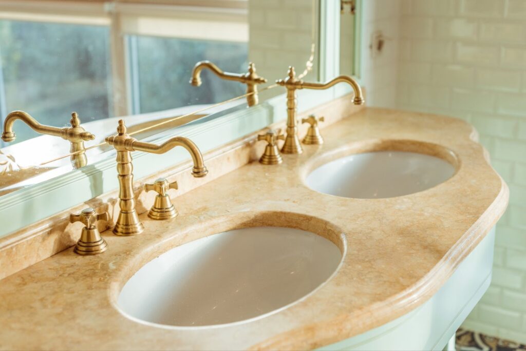 A luxurious bathroom with two marble gold sinks and a large mirror.