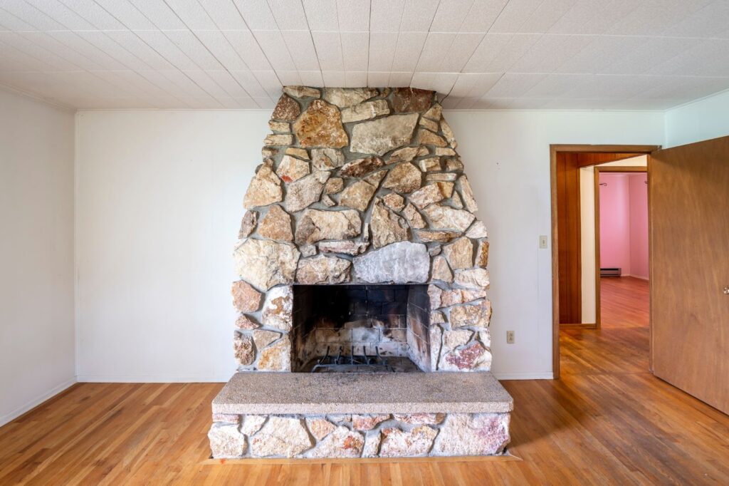 A stone fireplace with a mantel stands prominently in a living room adorned with rich hardwood flooring.